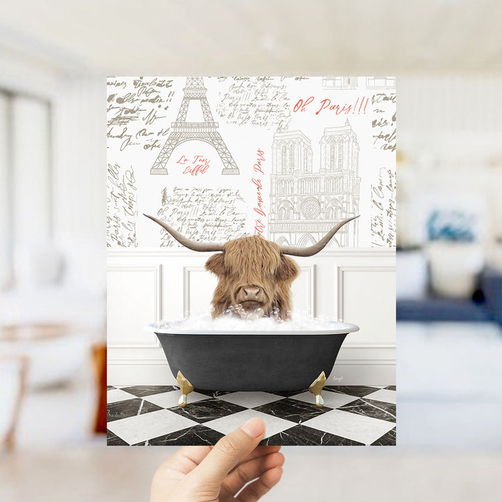 A hand is holding up a printed image featuring a horned animal, likely a yak or a similar animal, sitting in a bathtub filled with water, surrounded by various Paris-themed elements such as the Eiffel Tower and other landmarks.