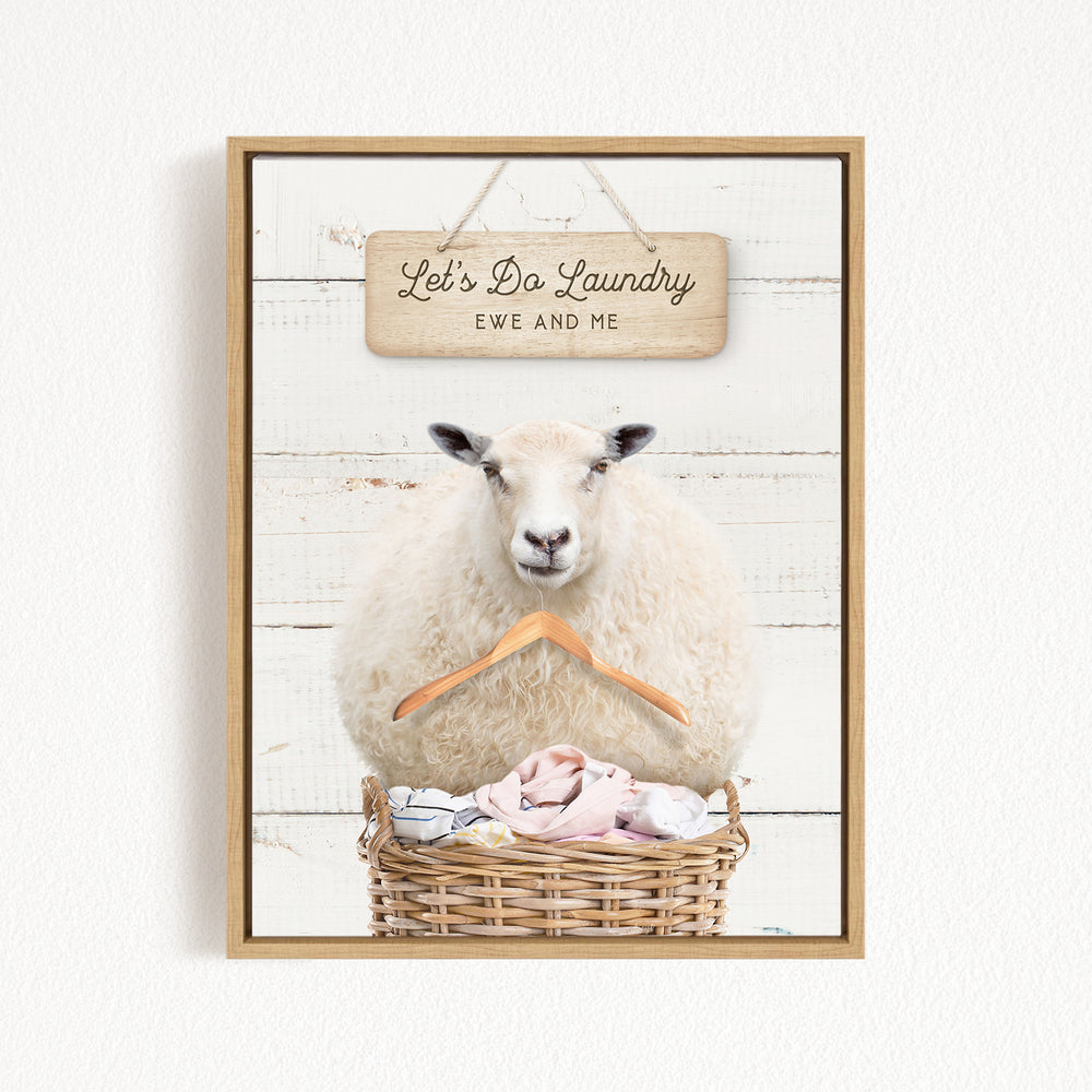 A white sheep sits in a wicker basket filled with laundry, with a wooden sign above that reads "Let's Da Laundry Ewe and Me".