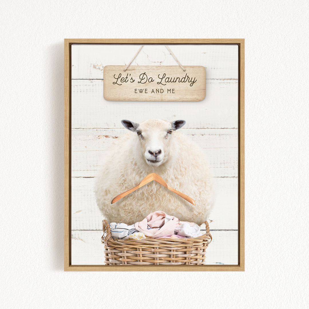 A white sheep sits in a wicker basket filled with laundry, with a wooden sign above that reads "Let's Da Laundry Ewe and Me".