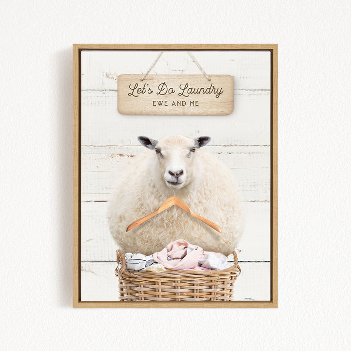 A white sheep sits in a wicker basket filled with laundry, with a wooden sign above that reads "Let's Da Laundry Ewe and Me".