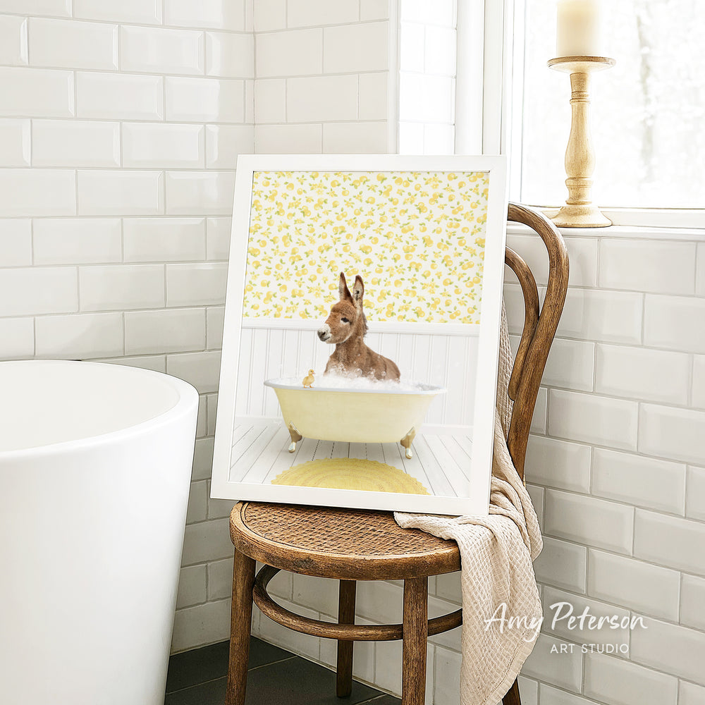 A framed image of a dog sitting in a bathtub, surrounded by yellow flowers, is displayed on a wooden chair in a bathroom setting.