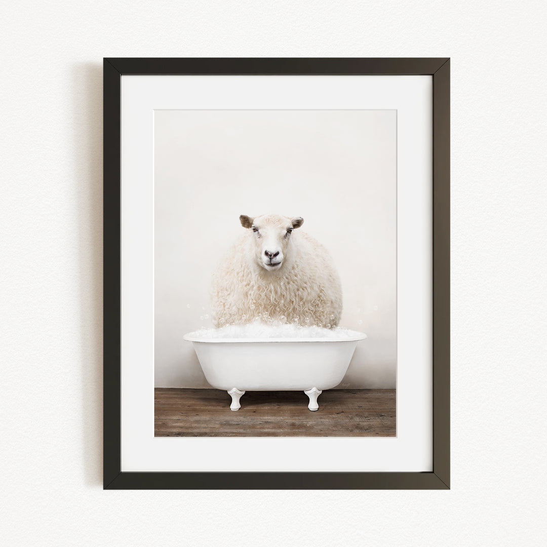 A fluffy white sheep sits in a white bathtub, surrounded by a wooden floor.