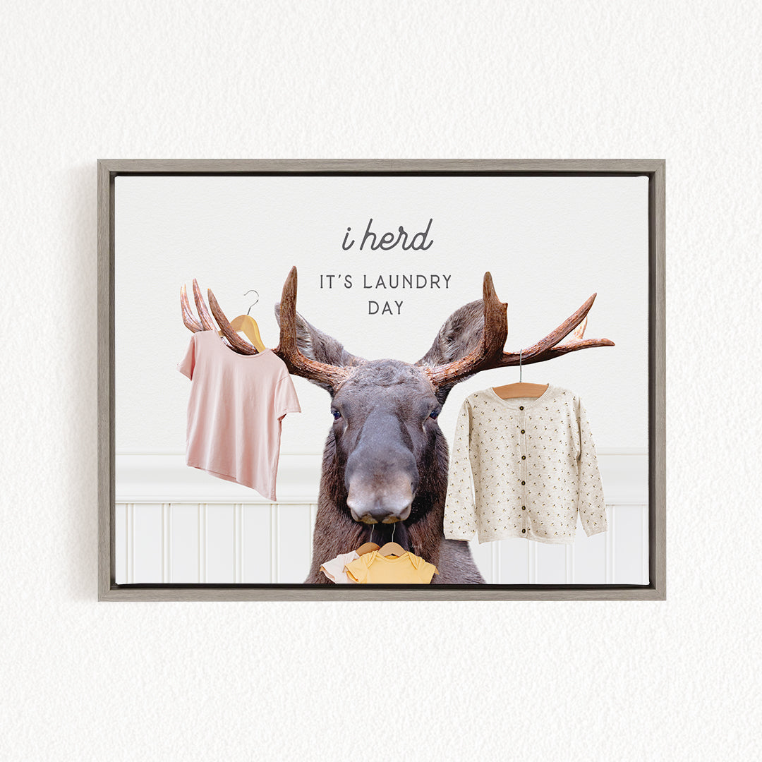 A framed image depicting a moose with antlers holding clothes, accompanied by the text "i herd, it's laundry day"