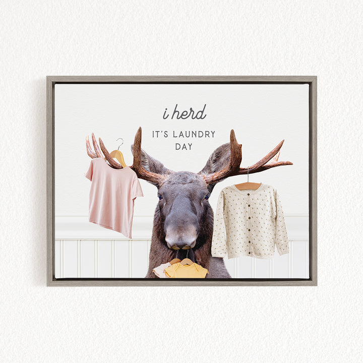 A framed image depicting a moose with antlers holding clothes, accompanied by the text "i herd, it's laundry day"