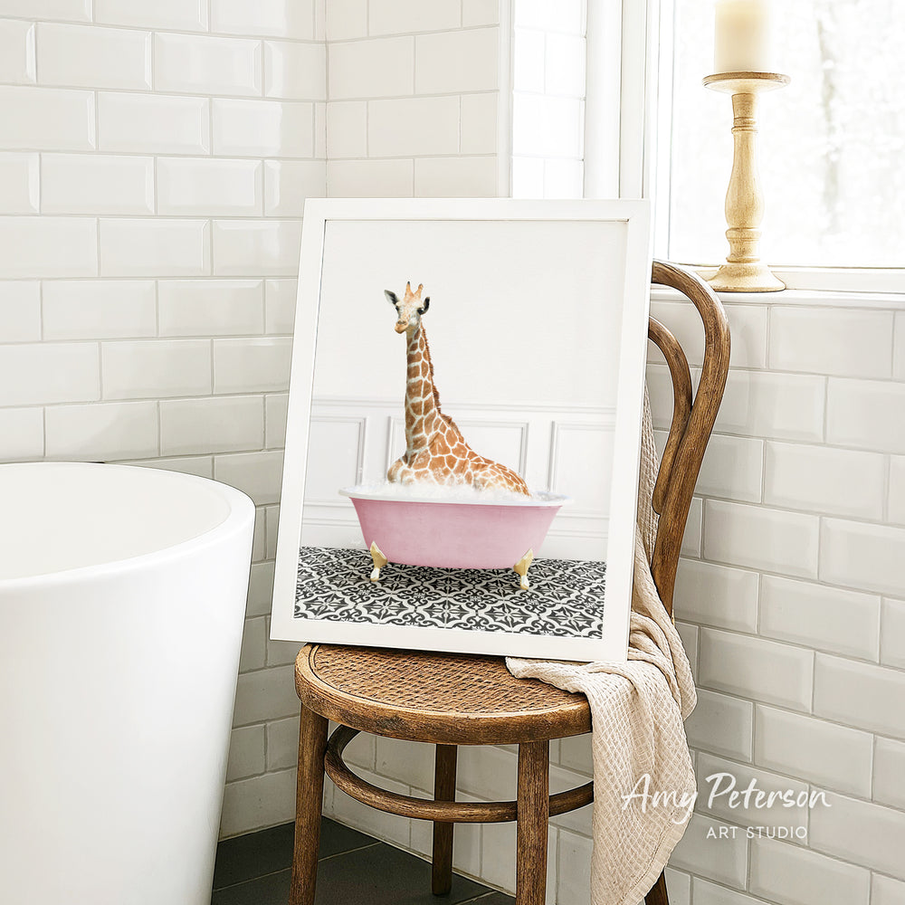 A framed image of a giraffe sitting in a pink bathtub is displayed on a wooden chair in a bathroom setting.
