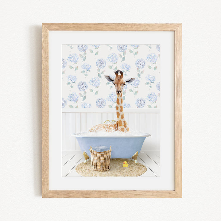 A giraffe is sitting in a blue bathtub filled with bubbles, surrounded by a wicker basket and yellow rubber ducks.