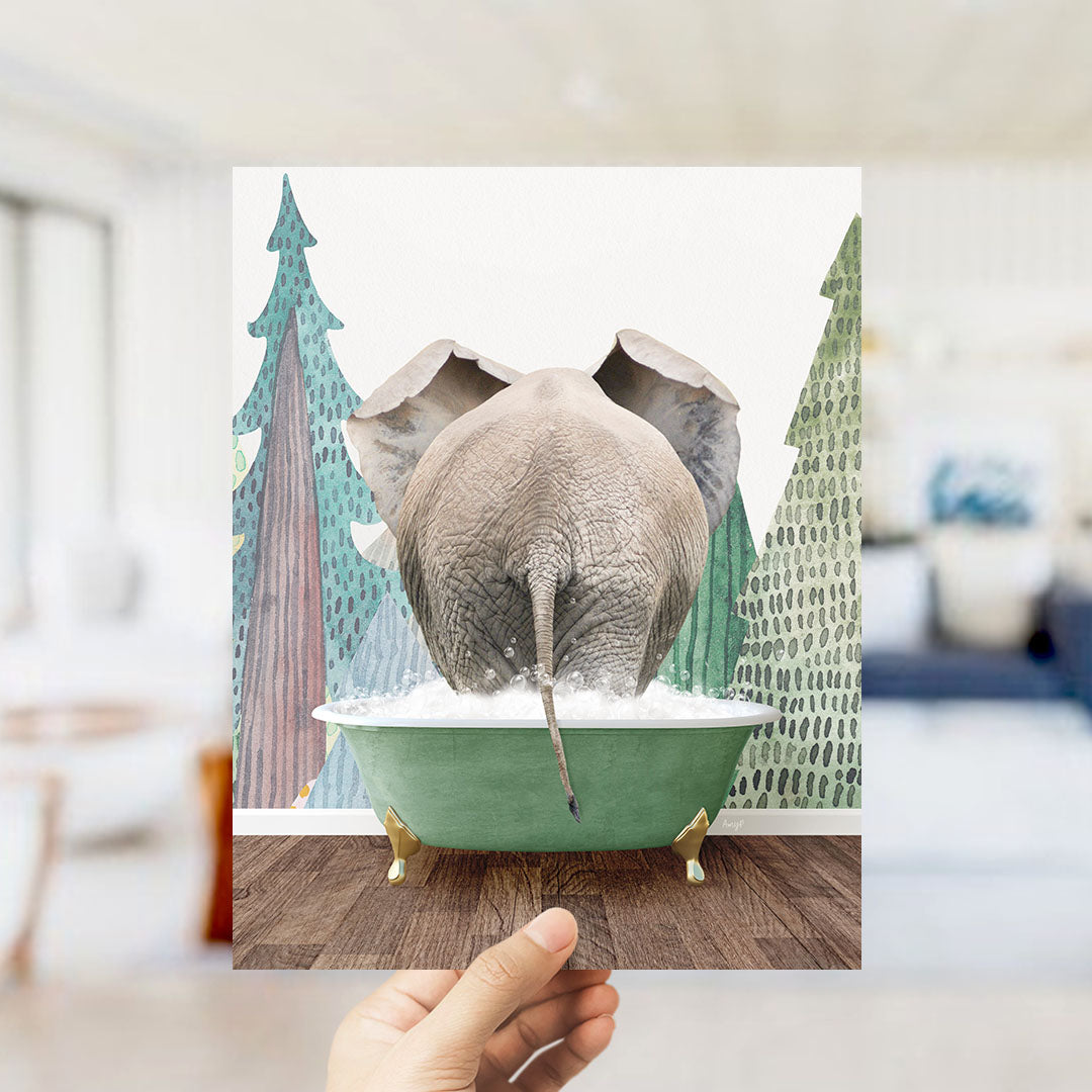 A hand holds up a framed image depicting an elephant sitting in a green bathtub, surrounded by trees with a snowy landscape.