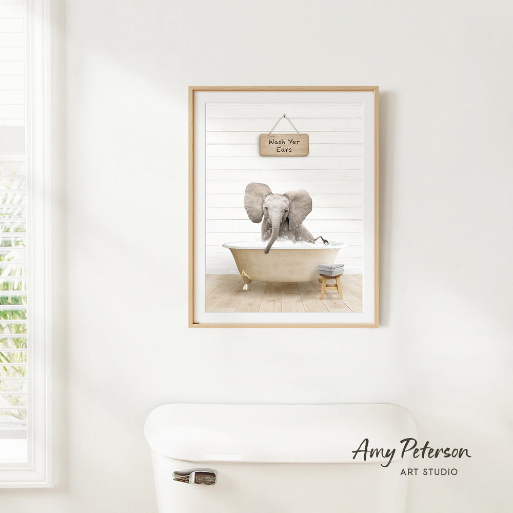 A framed print of an elephant sitting in a bathtub, with a sign above it that says "Wash Your Ears".