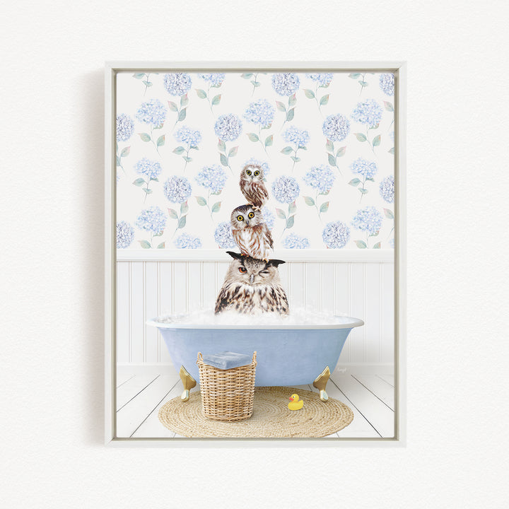 A framed image depicting three owls sitting in a bathtub filled with water, surrounded by a blue floral pattern on the wall.