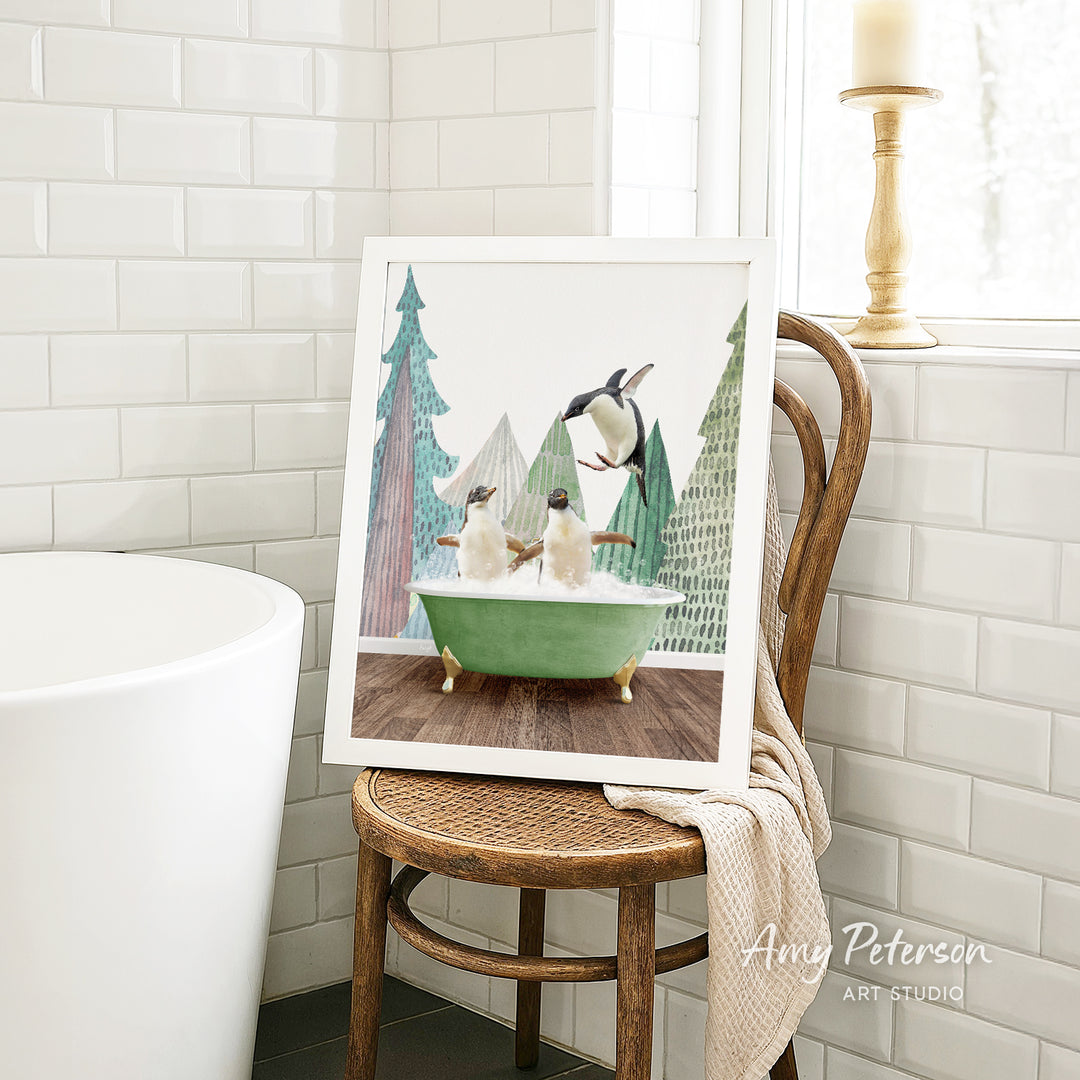 A framed painting of two penguins sitting in a green bathtub is displayed on a wooden chair in a bathroom setting.