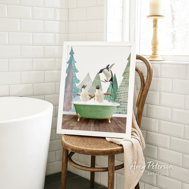 A framed painting of two penguins sitting in a green bathtub is displayed on a wooden chair in a bathroom setting.
