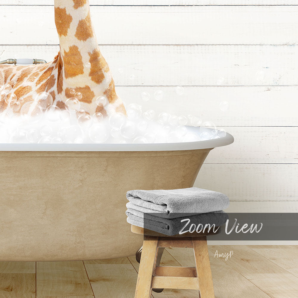 A giraffe standing in a bathtub filled with bubbles, with a towel and stool nearby.