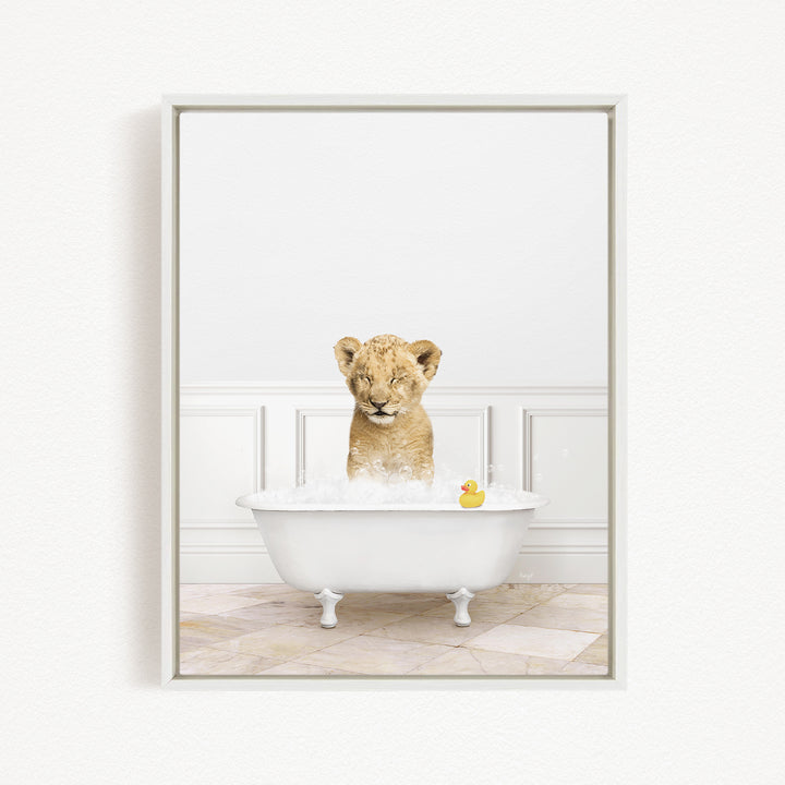 A young lion cub sitting in a white bathtub filled with bubbles, with a rubber duck floating nearby.