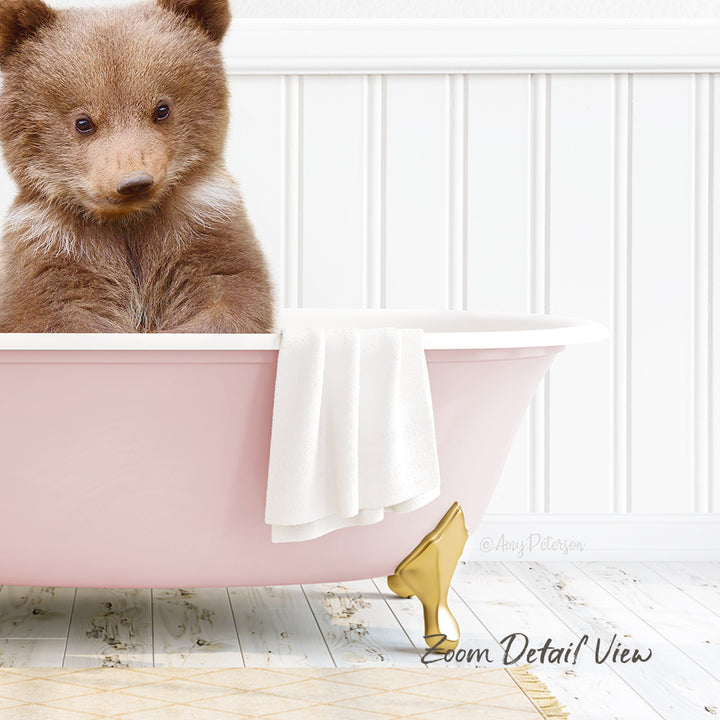 A cute brown bear sitting in a pink bathtub, with a white towel and gold bathtub leg visible.
