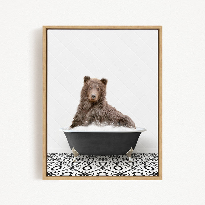 A brown bear sitting in a black bathtub filled with bubbles, looking directly at the camera.
