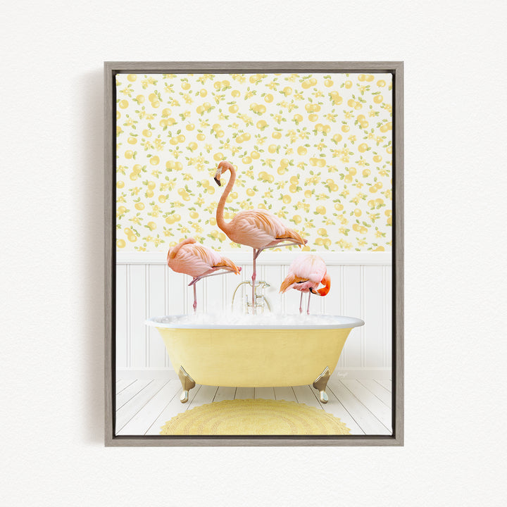 A framed image depicting three pink flamingos standing in a yellow bathtub, with a yellow and white floral wallpaper in the background.