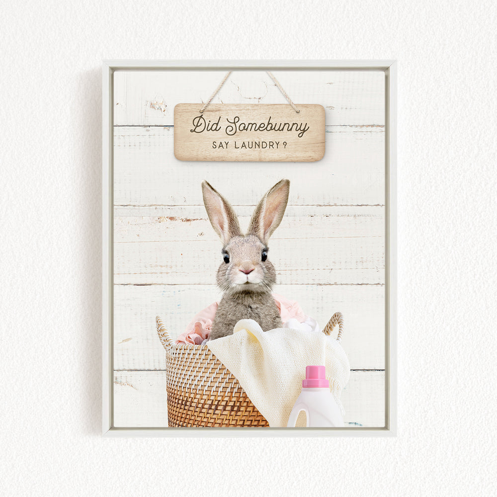 A cute rabbit sitting in a wicker basket filled with laundry, with a sign above that says "Did Somebunny Say Laundry?".