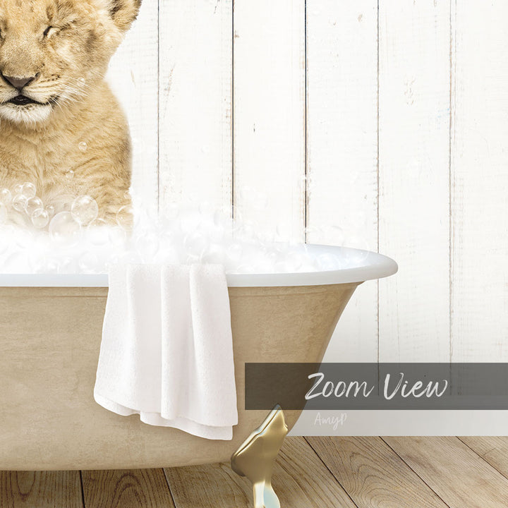 A lion cub is sitting in a bathtub filled with bubbles, with a towel draped over the side of the tub.