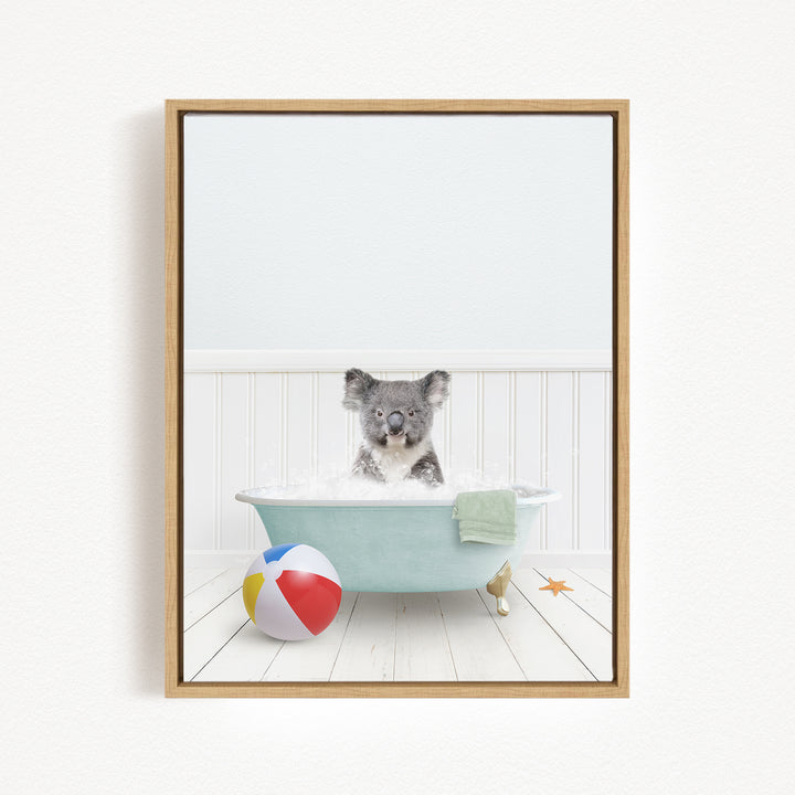 A koala bear sitting in a bathtub filled with bubbles, surrounded by a beach ball and a towel.