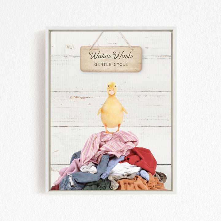 A yellow duck standing on a pile of colorful clothes, with a wooden sign above that reads "Warm Wash Gentle Cycle".