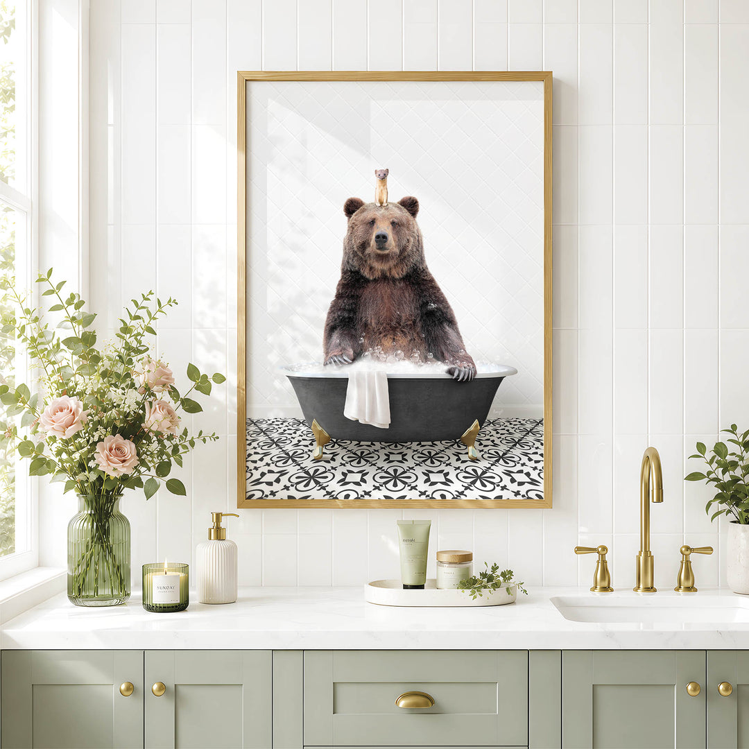 A framed image of a bear sitting in a bathtub, surrounded by flowers and candles, is displayed on a white tiled wall above a bathroom sink.