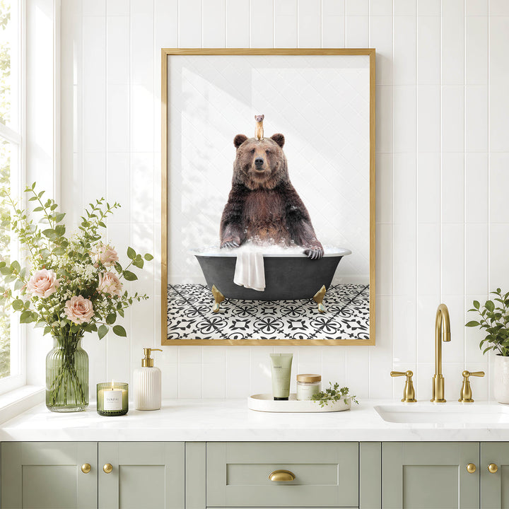 A framed image of a bear sitting in a bathtub, surrounded by flowers and candles, is displayed on a white tiled wall above a bathroom sink.