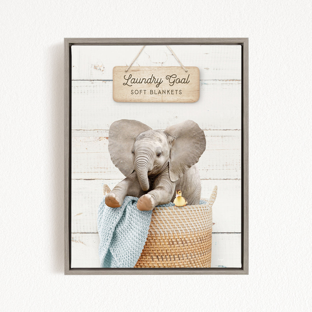 A gray elephant sitting in a woven basket, with a sign above that says "Laundry Goal Soft Blankets".