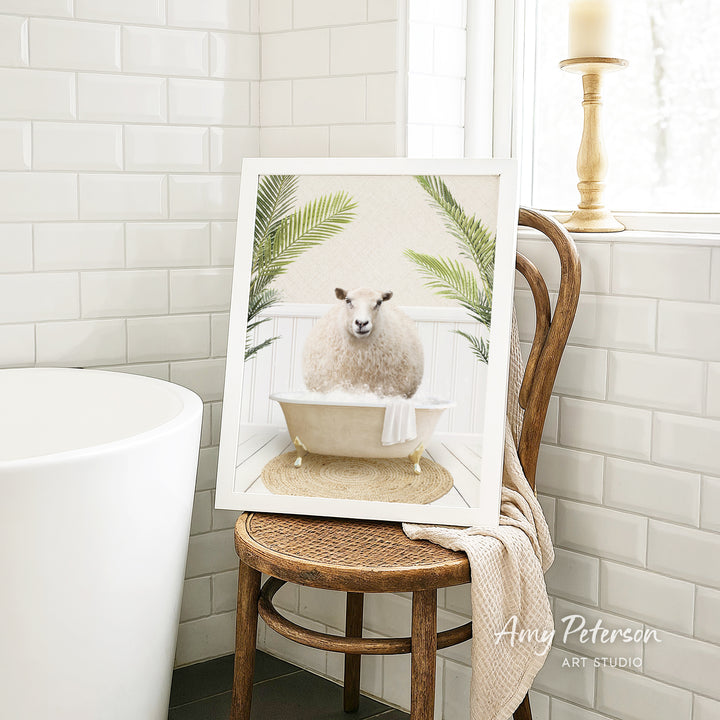 A framed image of a sheep sitting in a bathtub, surrounded by palm leaves, is displayed on a wooden chair in a bathroom setting.