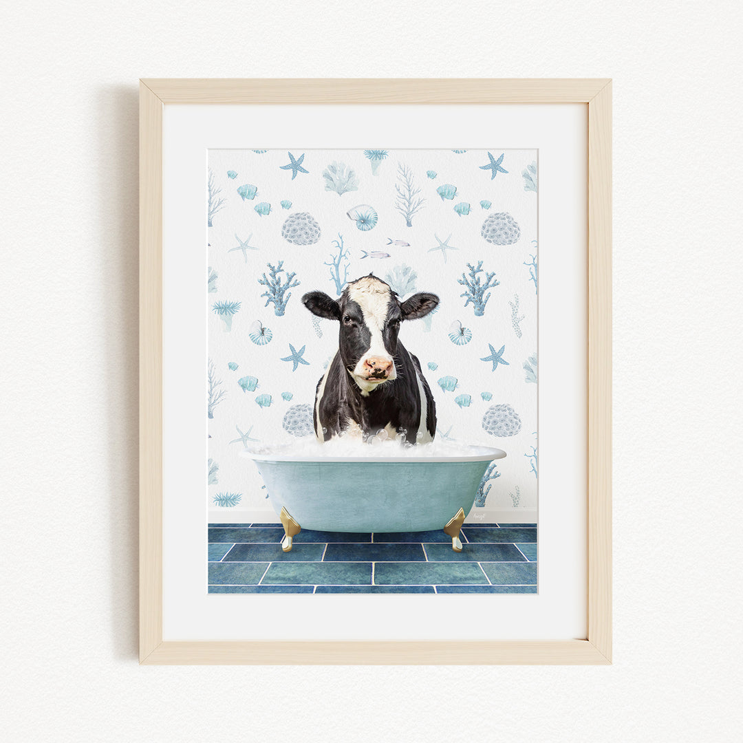 A framed image depicting a black and white cow sitting in a bathtub filled with bubbles, surrounded by a blue and white patterned wall.