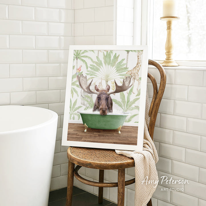 A framed image of a moose sitting in a bathtub is displayed on a wooden chair in a bathroom setting.
