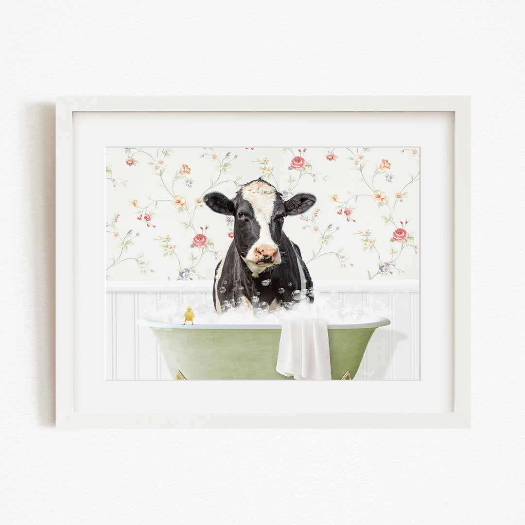 A black and white cow is sitting in a green bathtub filled with bubbles, with a floral wallpaper in the background.