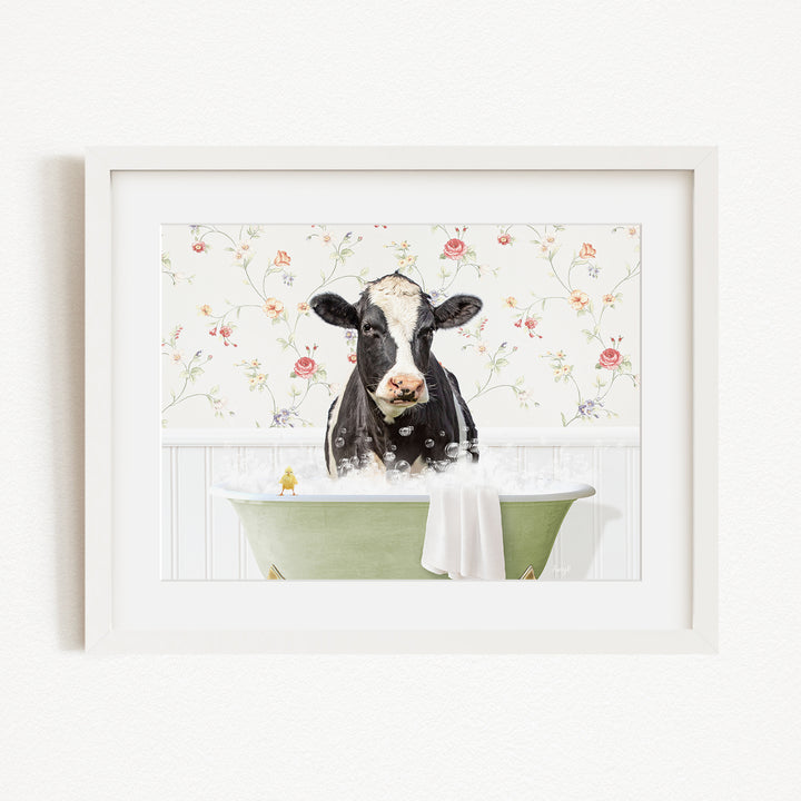 A black and white cow is sitting in a green bathtub filled with bubbles, with a floral wallpaper in the background.