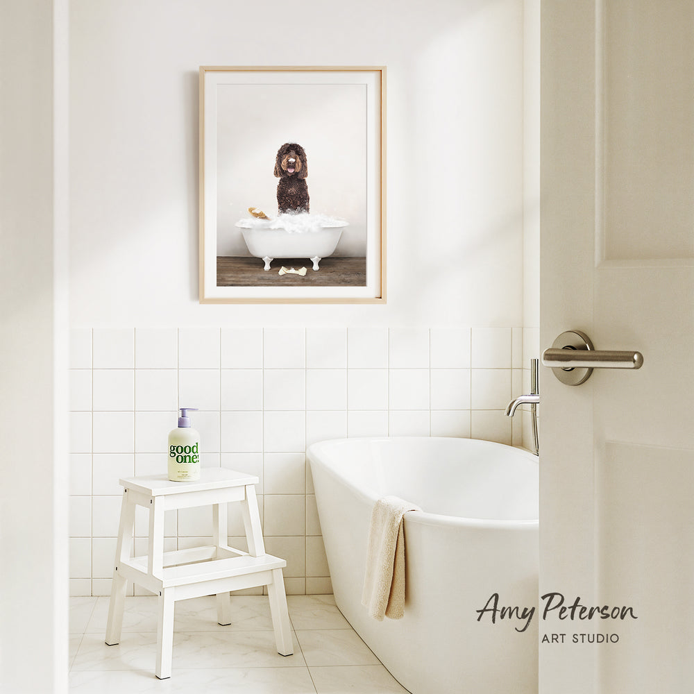 A framed image of a dog sitting in a bathtub, with a towel draped over the side of the tub, is displayed on the wall above a white bathtub in a clean, white-tiled bathroom.