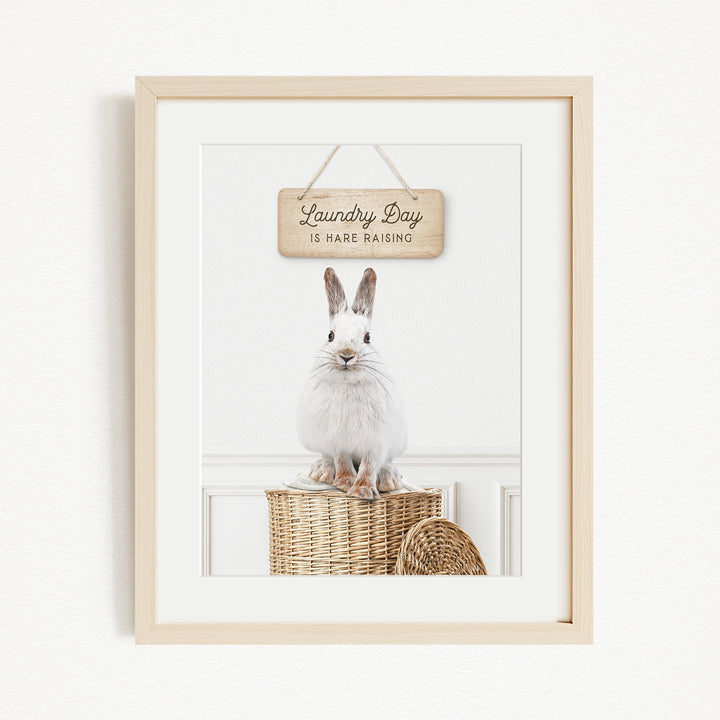 A white rabbit sitting on a wicker basket, with a wooden sign above it that says "Laundry Day is here raising".