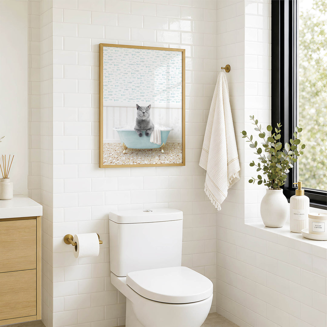 A bathroom with a white toilet, a framed picture of a cat sitting in a bathtub, and a window with greenery on the sill.