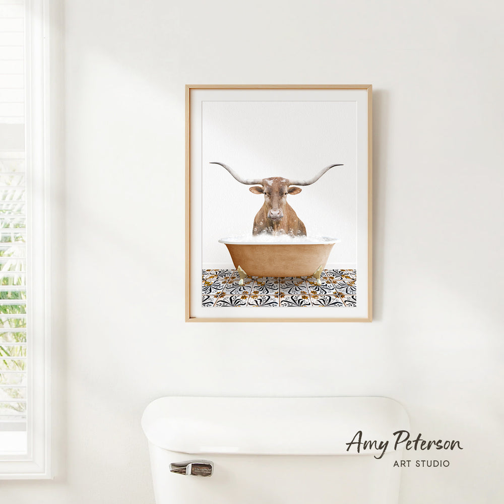 A framed image of a bull with long horns sitting in a bathtub, surrounded by a patterned tile design.