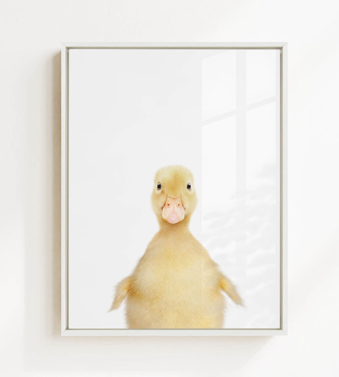 A cute yellow duck with a pink beak and eyes is looking directly at the camera in a white frame.