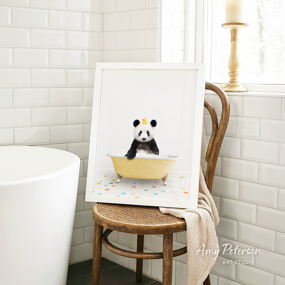 A framed image of a panda bear sitting in a bathtub, with a towel draped over the back of a chair in a bathroom setting.