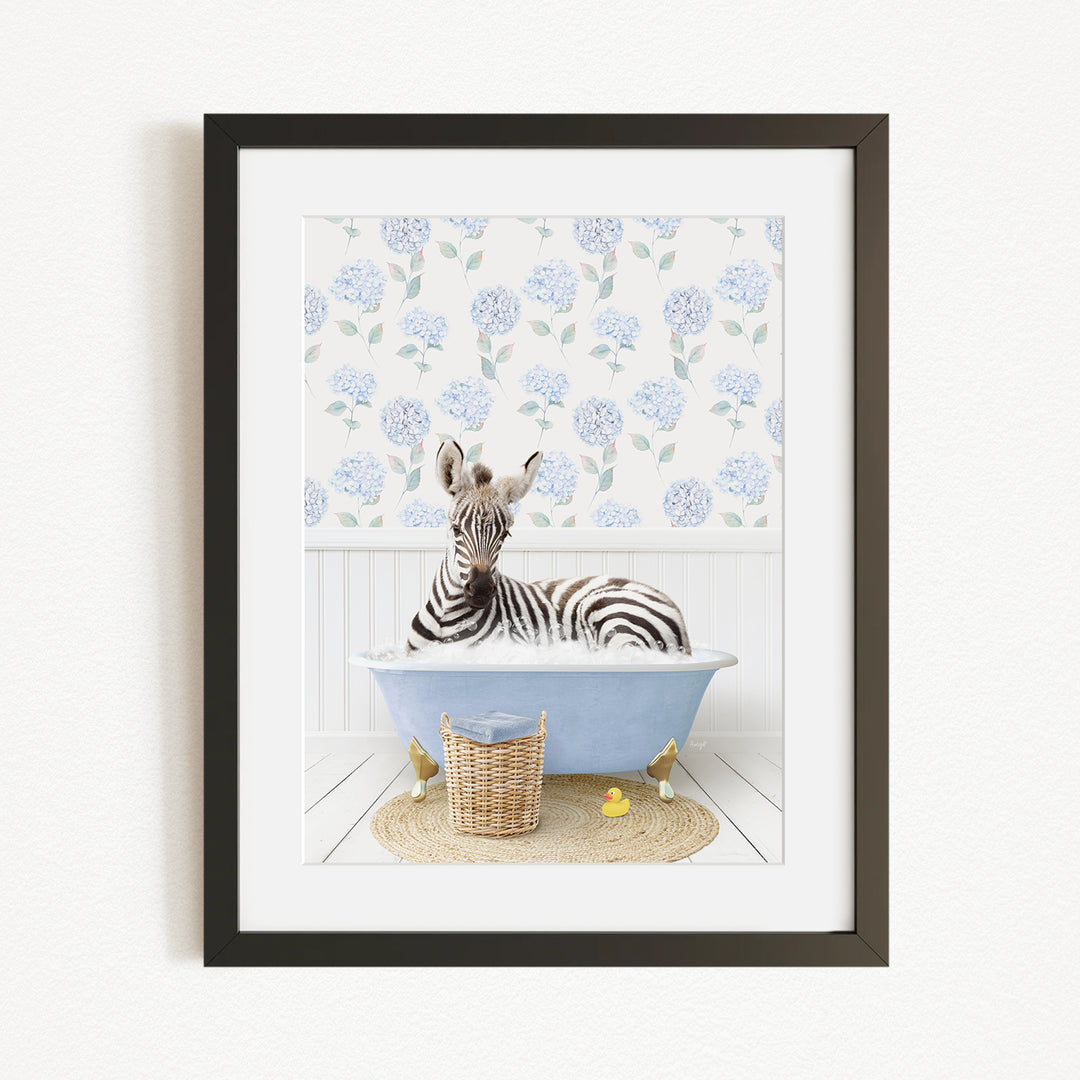 A zebra is sitting in a blue bathtub filled with water, surrounded by a wicker basket and yellow rubber ducks.