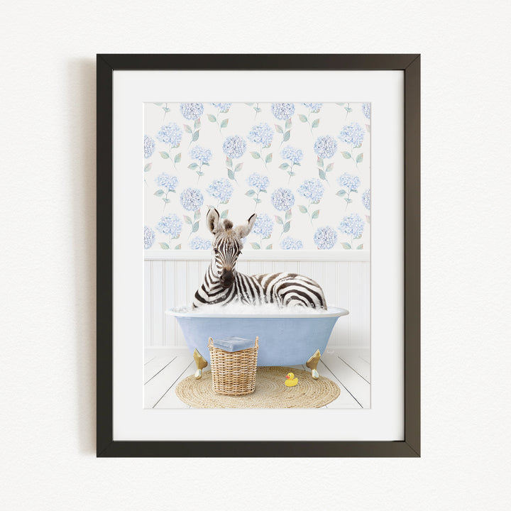 A zebra is sitting in a blue bathtub filled with water, surrounded by a wicker basket and yellow rubber ducks.