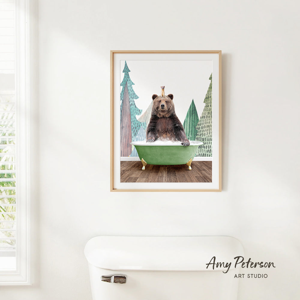 A framed print of a bear sitting in a green bathtub, surrounded by pine trees, is hanging on a white wall.