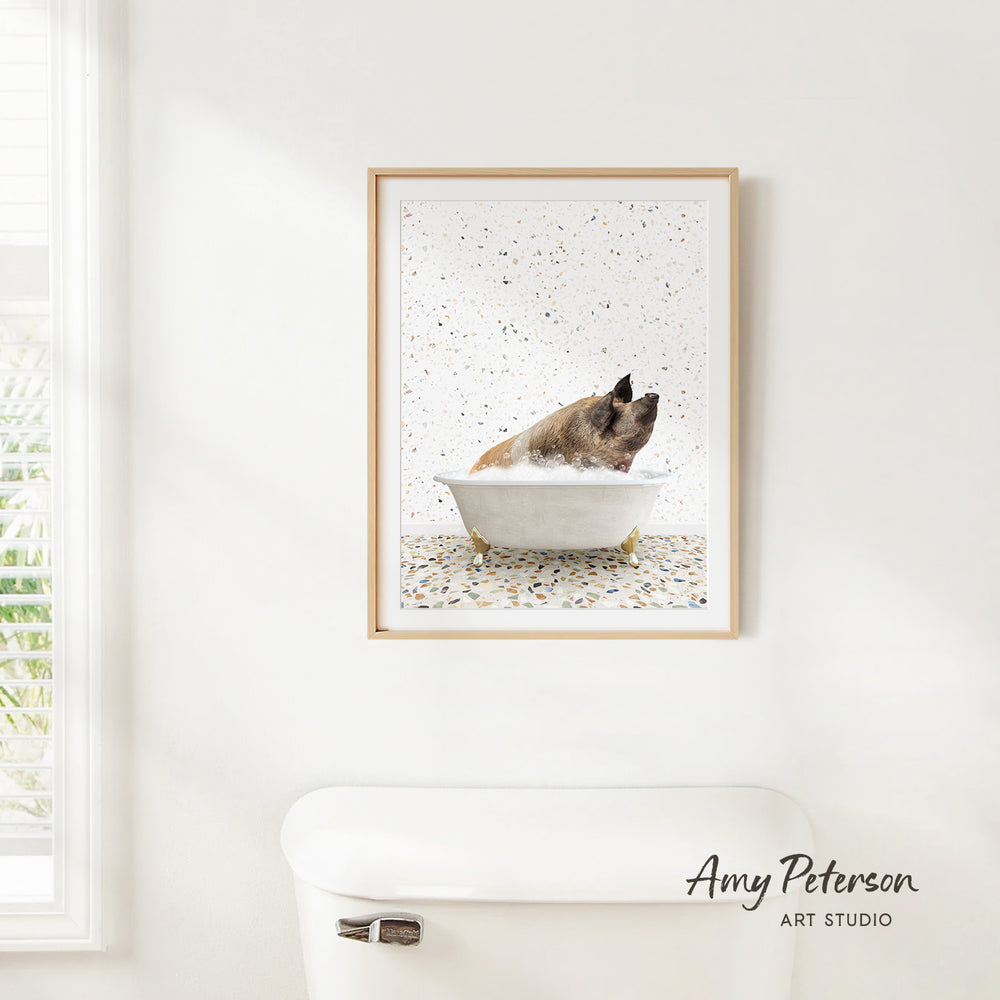 A framed image of a pig sitting in a bathtub, surrounded by a speckled background, is hanging on a white wall in a bathroom.