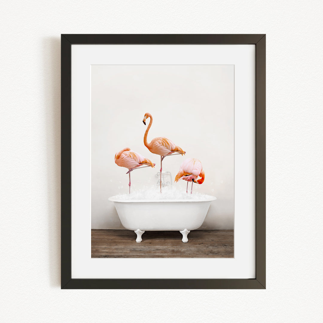 A framed image of three flamingos standing in a white bathtub filled with water.