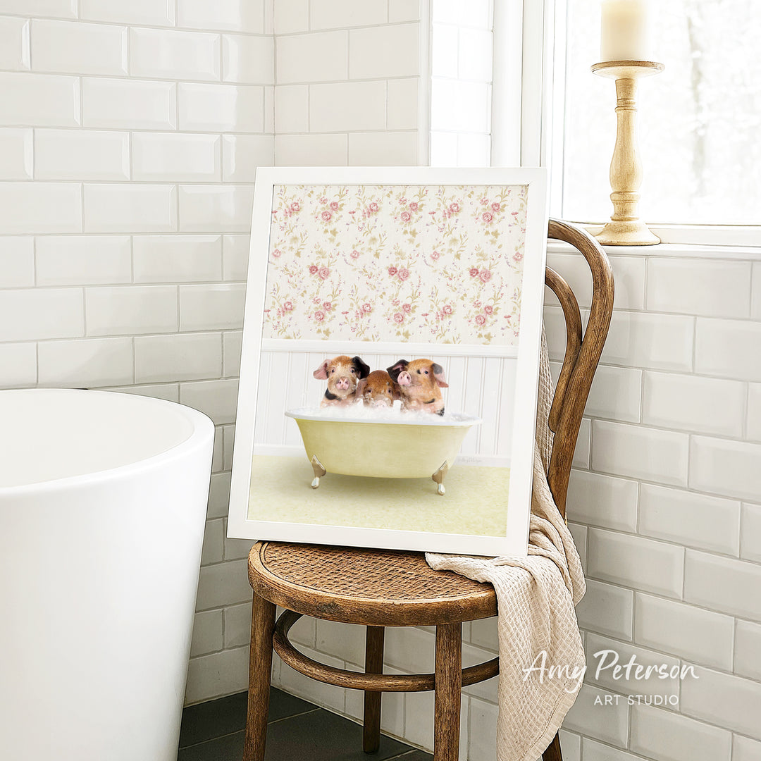 A framed image of two adorable pigs sitting in a bathtub, surrounded by a floral pattern, is displayed on a wooden chair in a bathroom setting.