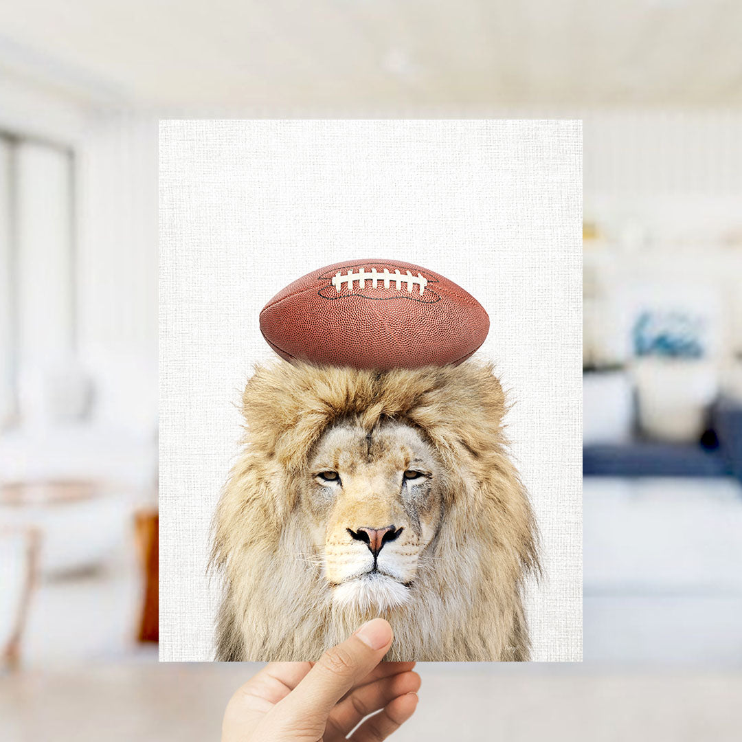 A hand holds up a framed image of a lion with a football on its head.