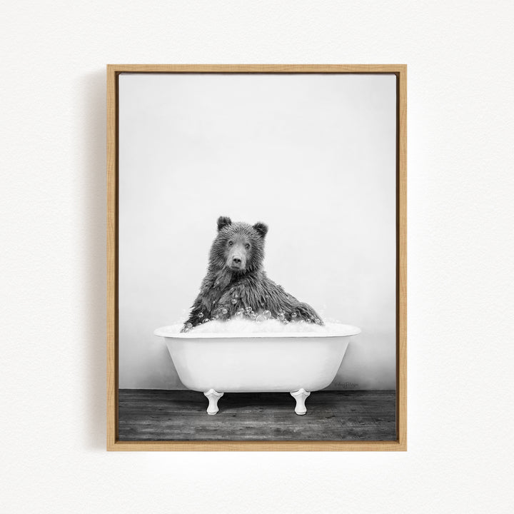 A black and white photograph of a bear sitting in a bathtub filled with water.