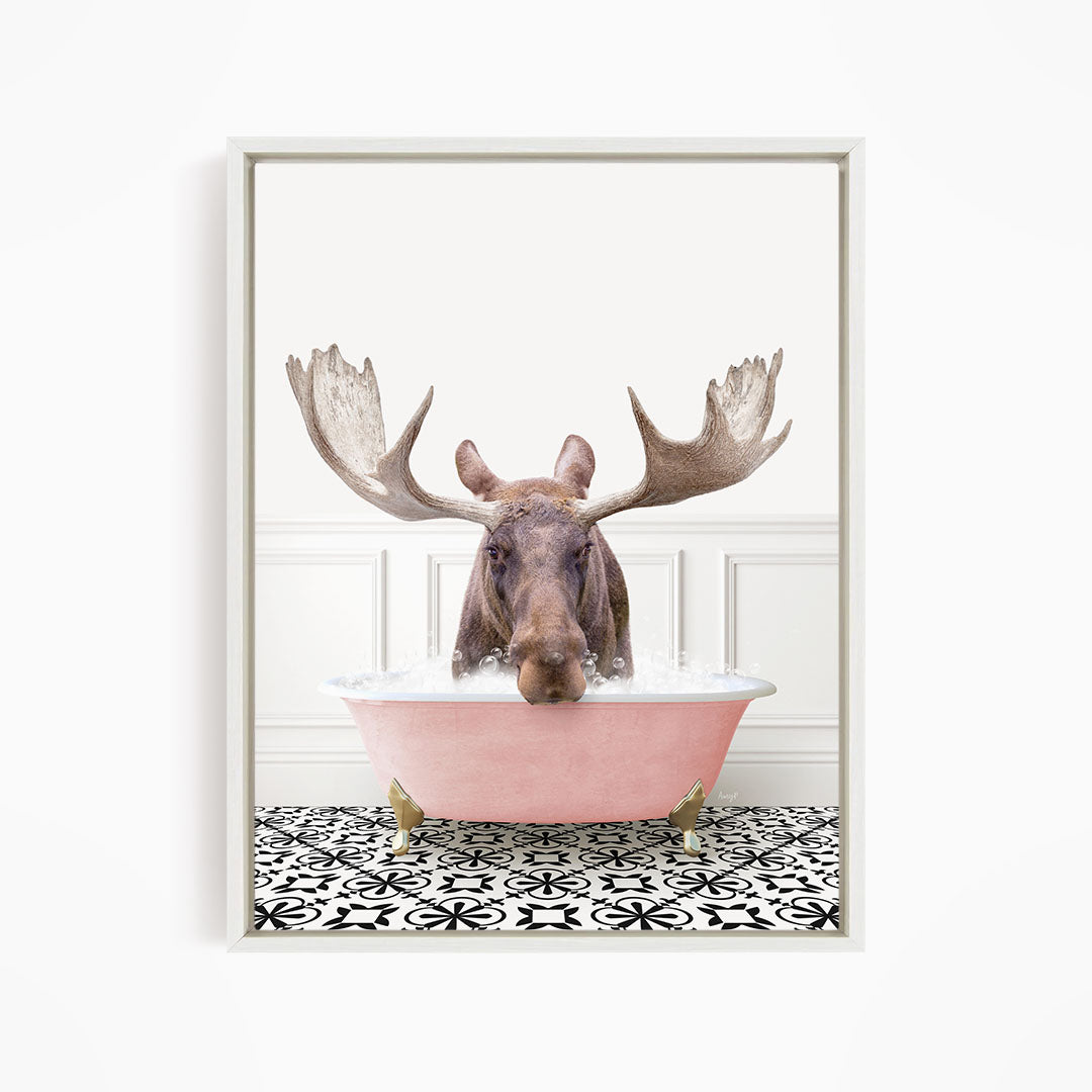 A moose with large antlers is sitting in a pink bathtub filled with water, surrounded by a black and white patterned floor.