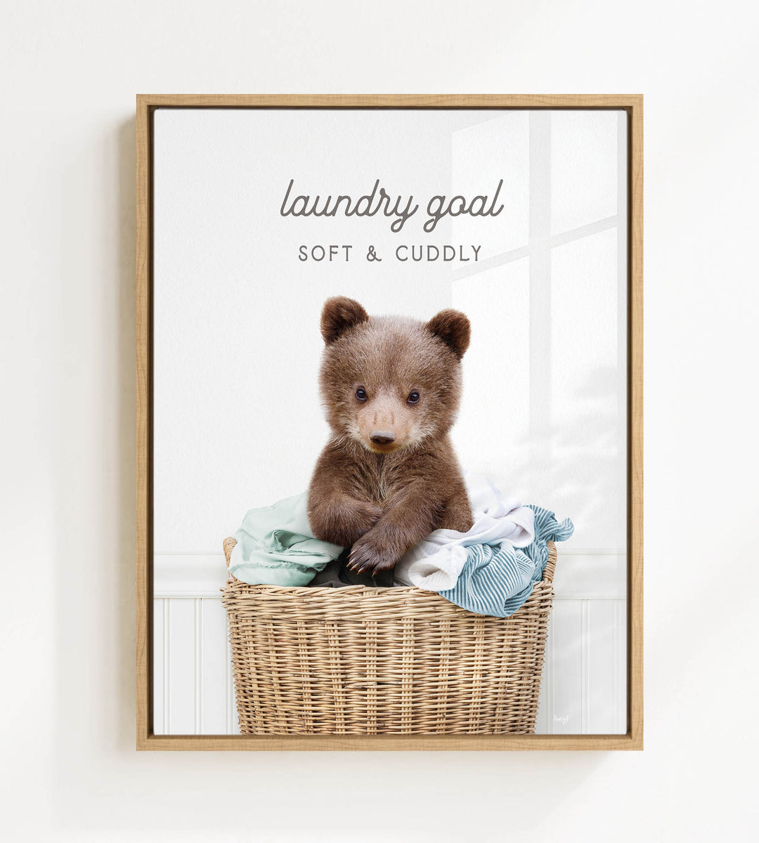 A cute brown bear sitting in a wicker laundry basket filled with clothes, with the text "laundry goal" and "soft & cuddly" written above it.