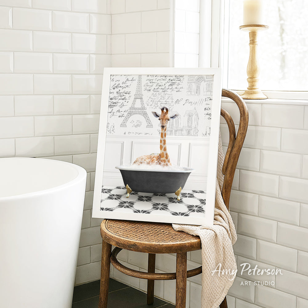 A framed image of a giraffe sitting in a bathtub, surrounded by a tiled pattern, is displayed on a wooden chair in a bathroom setting.