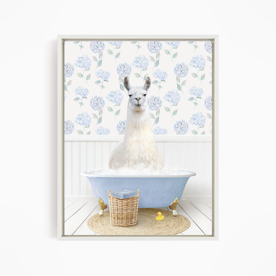 A white llama sitting in a blue bathtub filled with bubbles, surrounded by a wicker basket and a yellow rubber duck.
